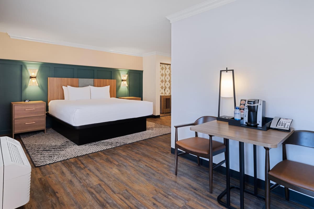 A hotel room with a bed, bedside table, lamp, desk, chair, and a coffee machine.