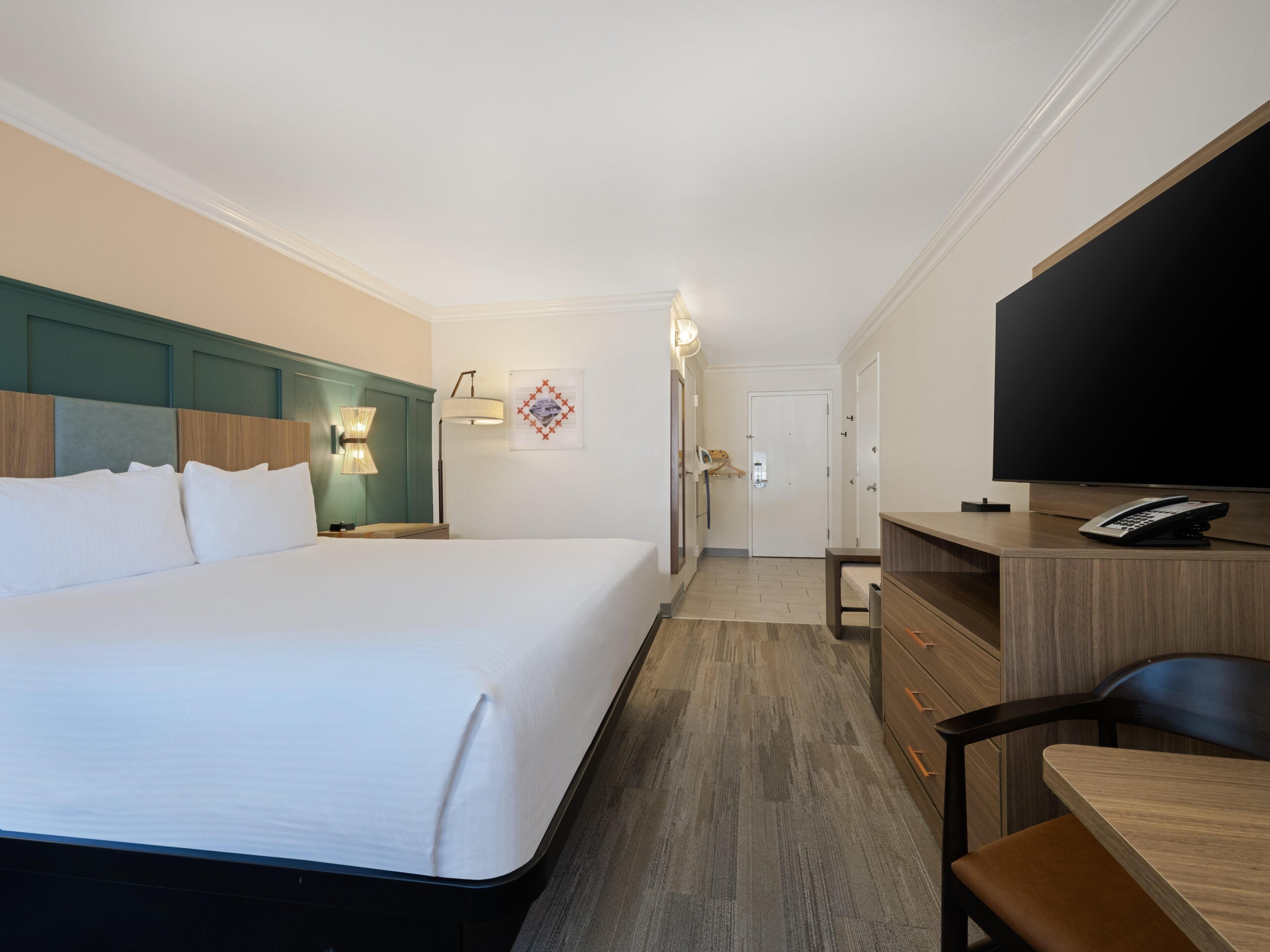 Een hotelkamer met een groot bed, een bureau met een telefoon, een televisie en een deur naar een badkamer.