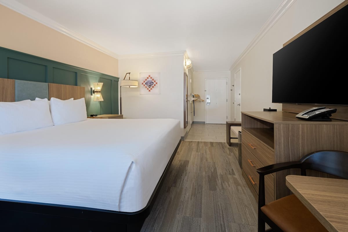 A hotel room with a large bed, a desk with a telephone, a television, and a door leading to a bathroom.