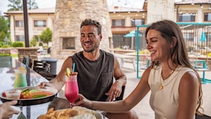 A couple dining outdoors at a restaurant with a stone pillar and a pool in the background.