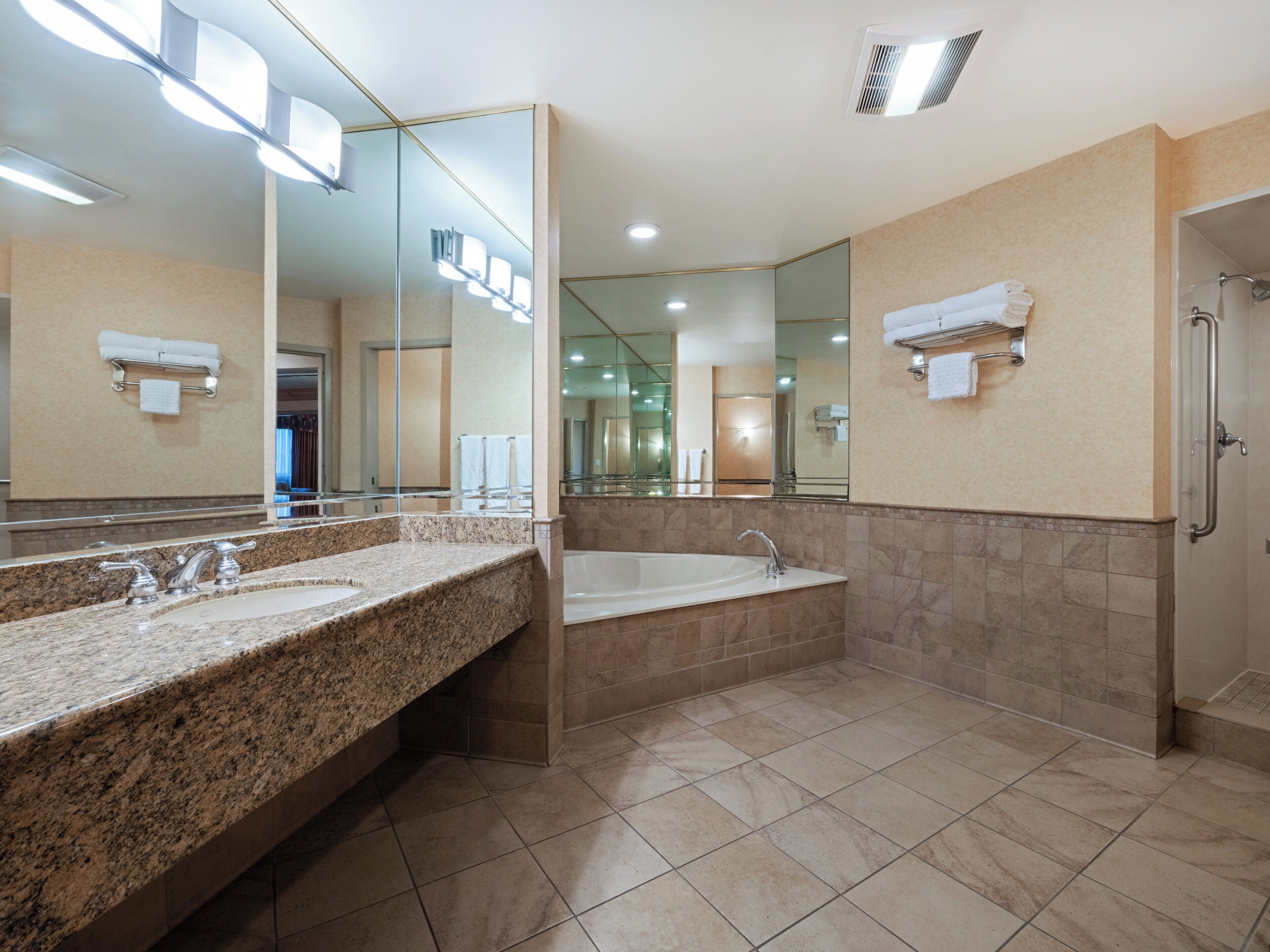 A modern bathroom with granite countertops, a large mirror, a bathtub, and a shower.