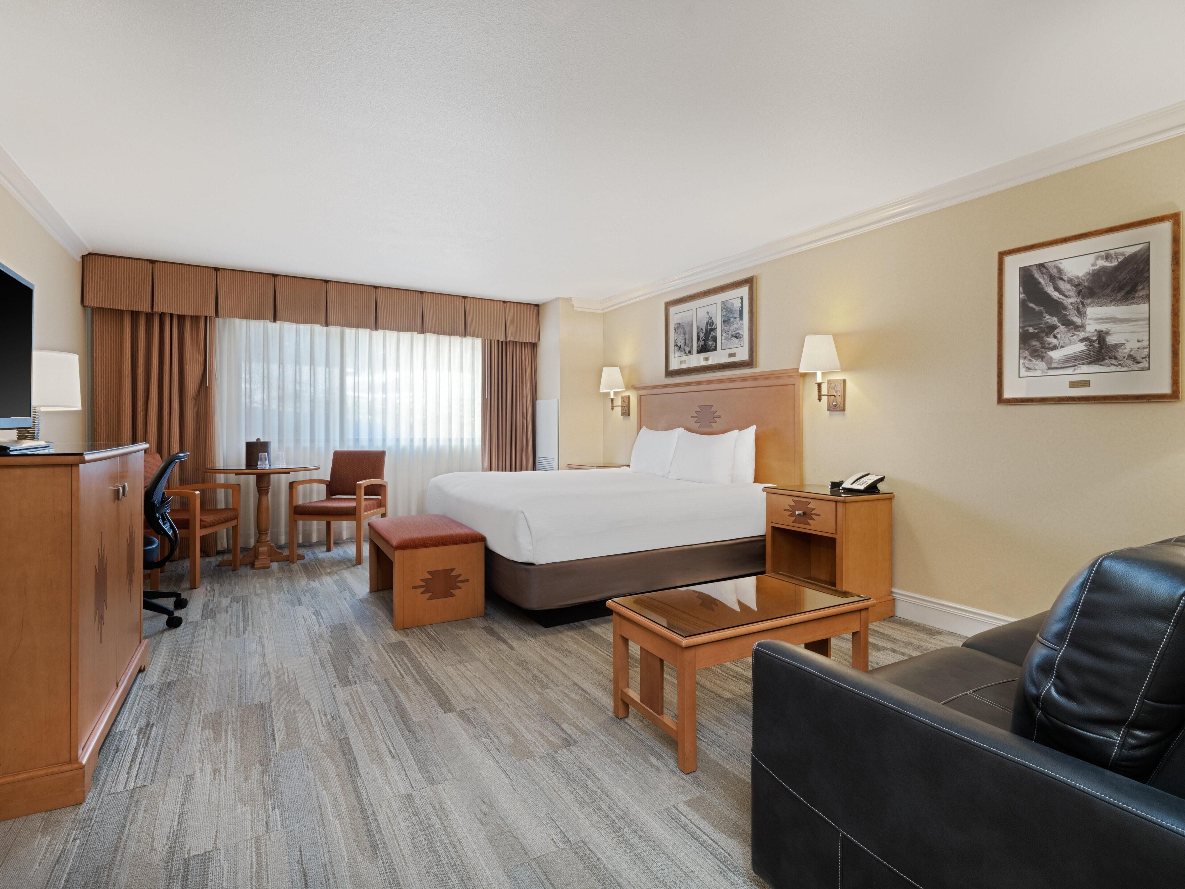 Hotelkamer met een bed, bureau, stoel, bank, televisie en raam met gordijnen.