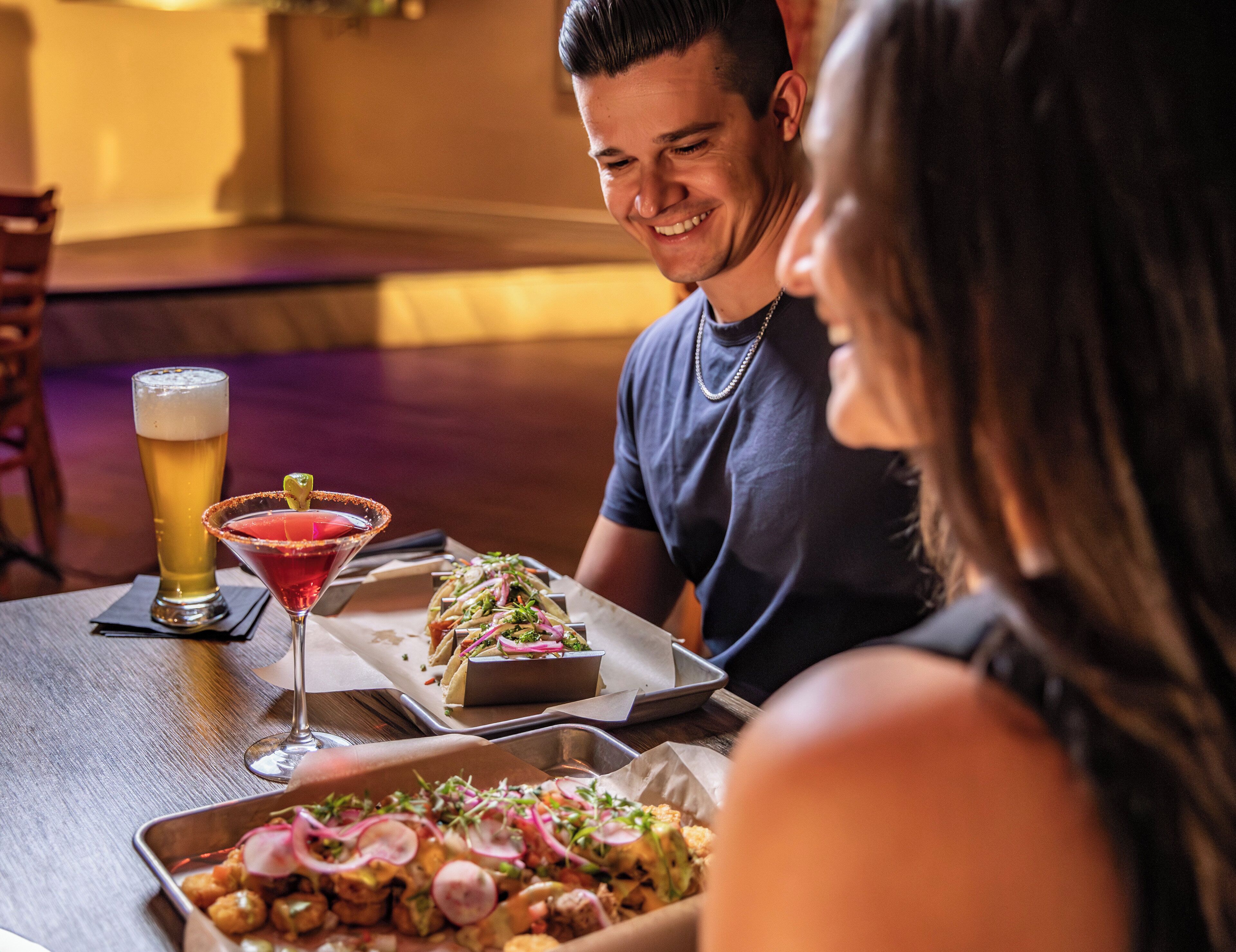 A dining table with food, drinks, and a tray of tacos.