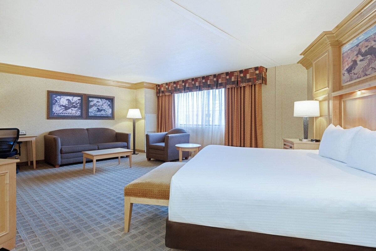 Habitación de hotel con una cama grande, un sofá, una silla, una mesita y un escritorio con lámpara.