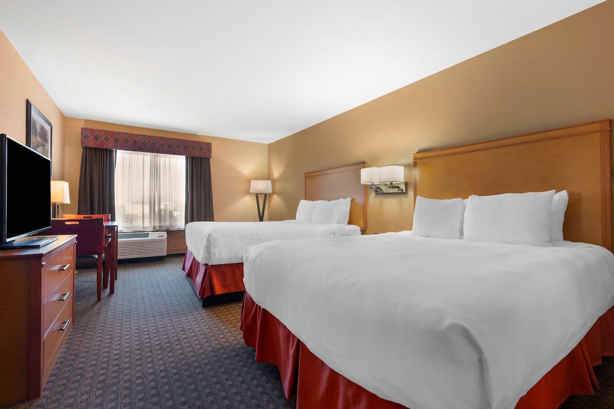 A hotel room with two beds, a desk with a television, a lamp, and a window with curtains.