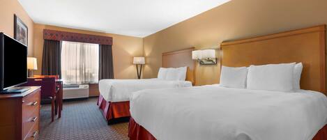Quarto de hotel com duas camas, uma mesa de trabalho com televisão, uma luminária e uma janela com cortinas.