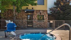 A hot tub with a metal railing, a blue chair, and a stone wall with a window. - Best Western Plus Olympic Inn (Klamath Falls)