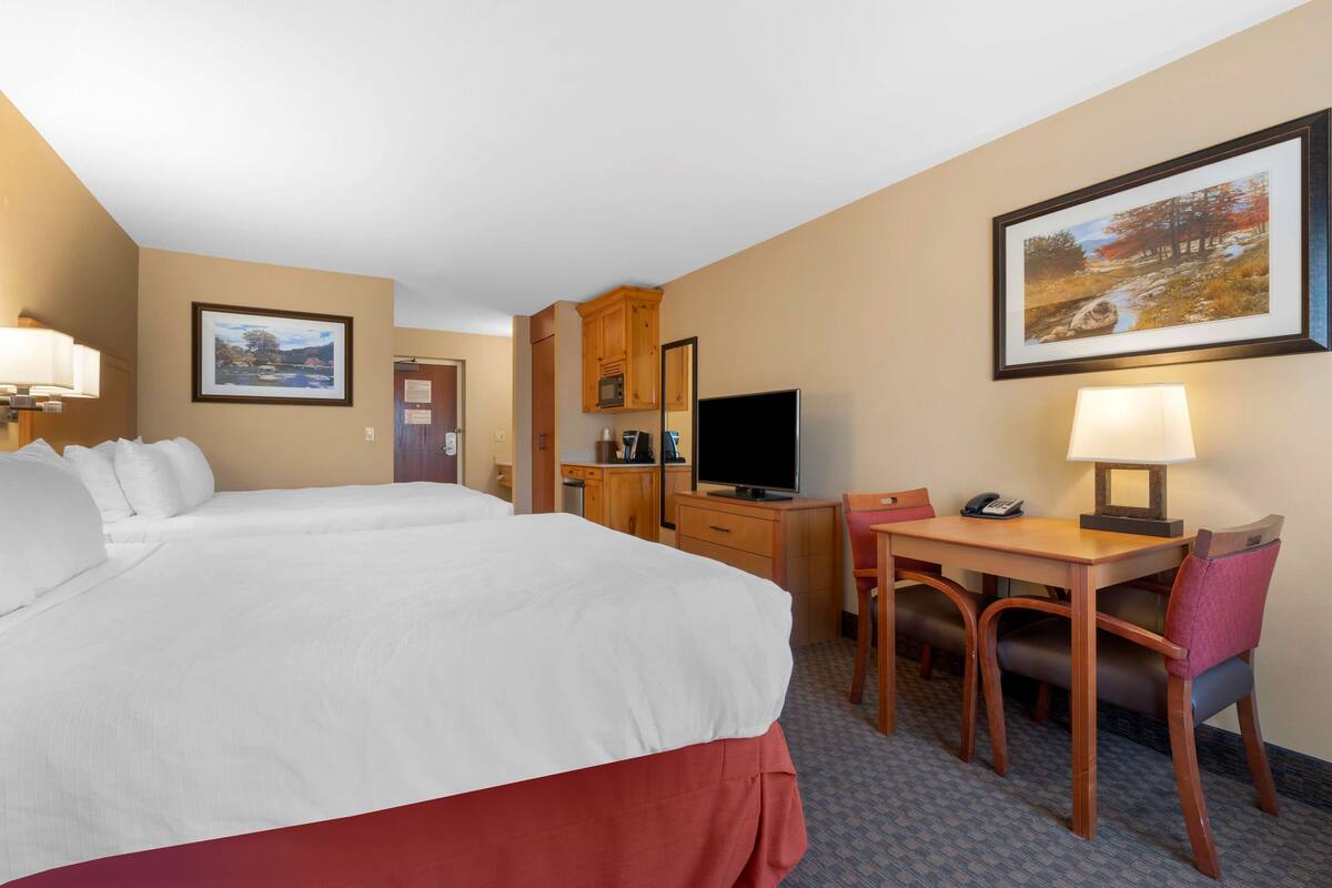 A hotel room with two beds, a desk with a chair, a television, and a painting on the wall.
