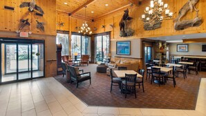 A spacious lobby with wooden walls, a chandelier, and a fireplace. There are multiple seating areas with tables and chairs. - Best Western Plus Olympic Inn (Klamath Falls)