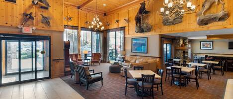 A spacious lobby with wooden walls, a chandelier, and a fireplace. There are multiple seating areas with tables and chairs.