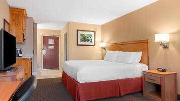 Habitación de hotel con cama, escritorio con televisor, mesita de noche y puerta que da a otra habitación.