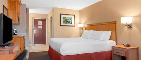 A hotel room with a bed, a desk with a television, a nightstand, and a door leading to another room.
