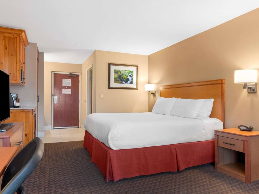 Habitación de hotel con cama, escritorio con televisor, mesita de noche y puerta que da a otra habitación.