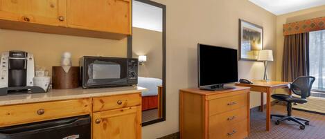 Habitación de hotel con armarios de madera, microondas, cafetera, televisión, escritorio y una silla.