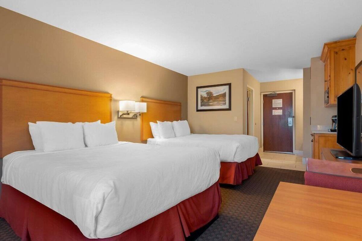A hotel room with two beds, a desk, a television, and a door.