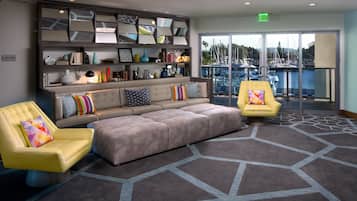 A lobby with a sectional sofa, two armchairs, a bookshelf, and a view of a marina through large glass doors.