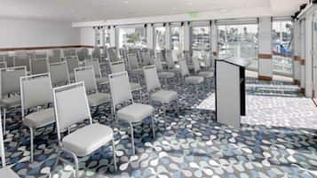 Un salón de conferencias con filas de sillas, un atril y grandes ventanales que ofrecen vistas al exterior.
