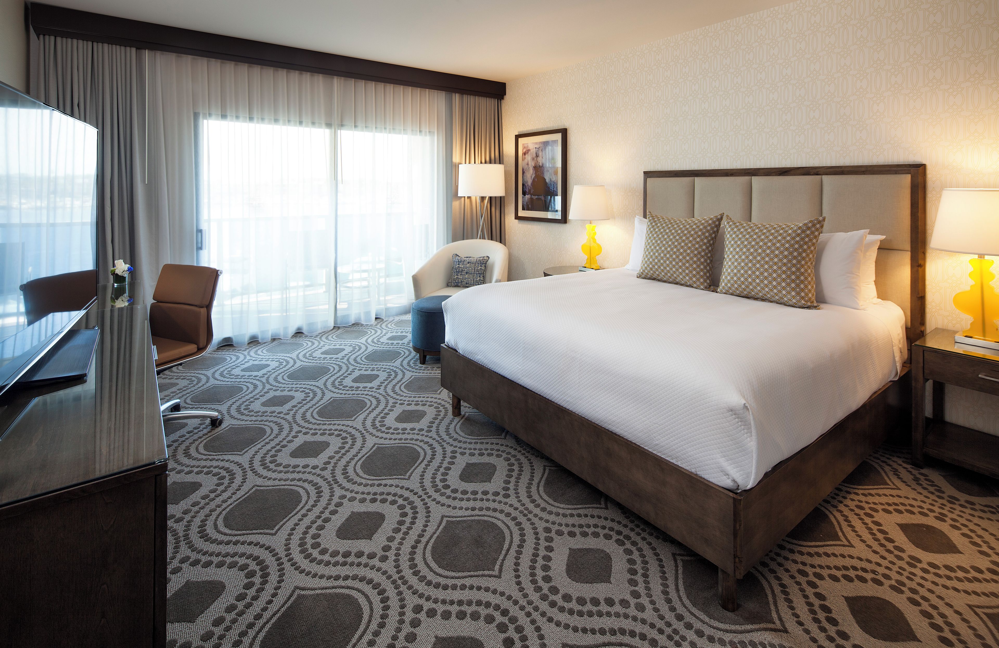 A hotel room with a large bed, a desk, a chair, a lamp, and a painting on the wall.