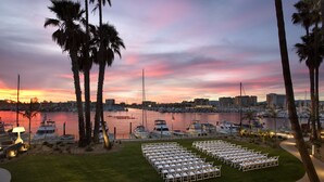 A sunset view of a marina with boats, palm trees, and a row of white chairs arranged for an event. - Marina del Rey Hotel (Marina del Rey)