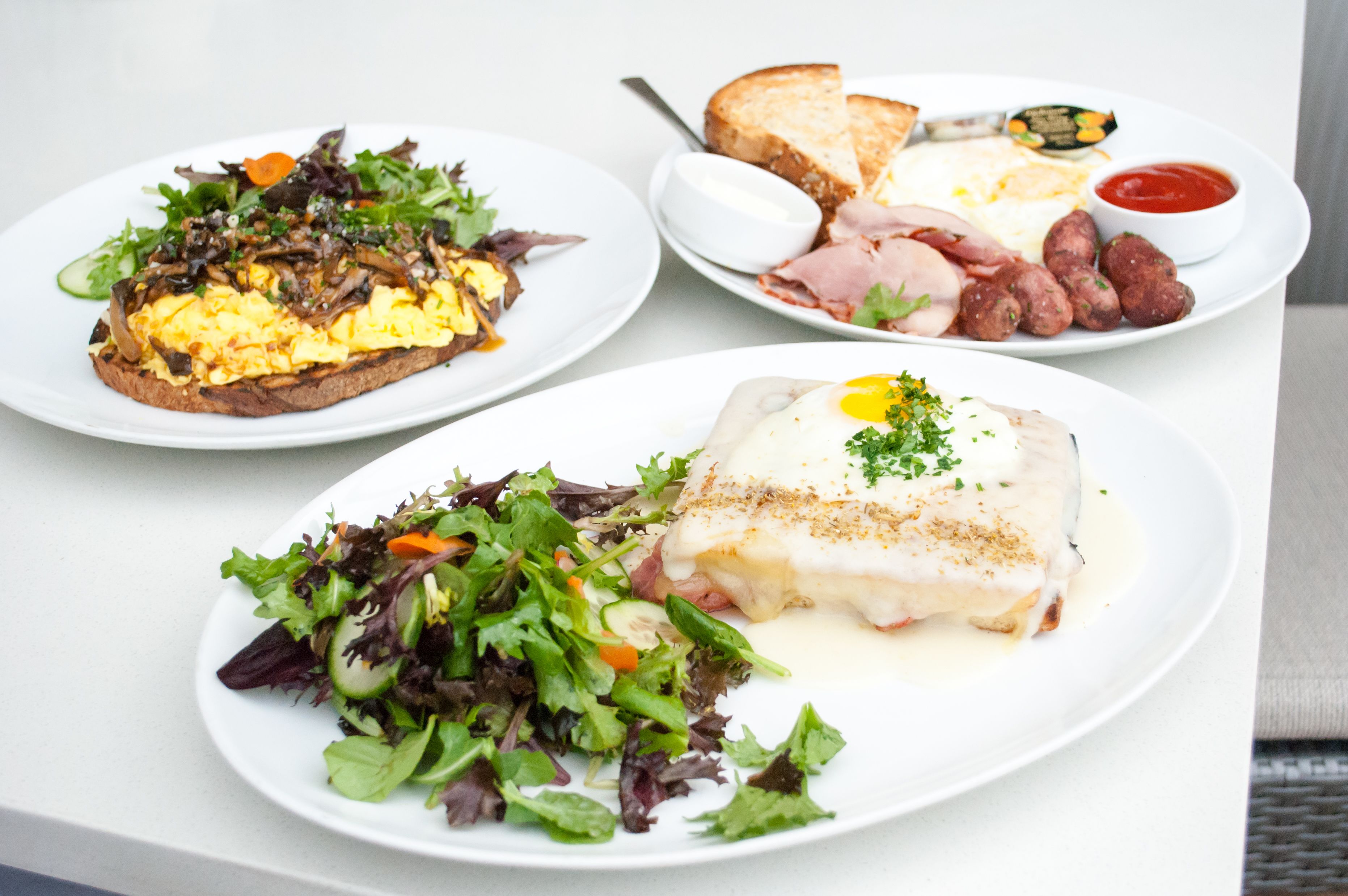 Three plates of food with various dishes including eggs, toast, and salads.