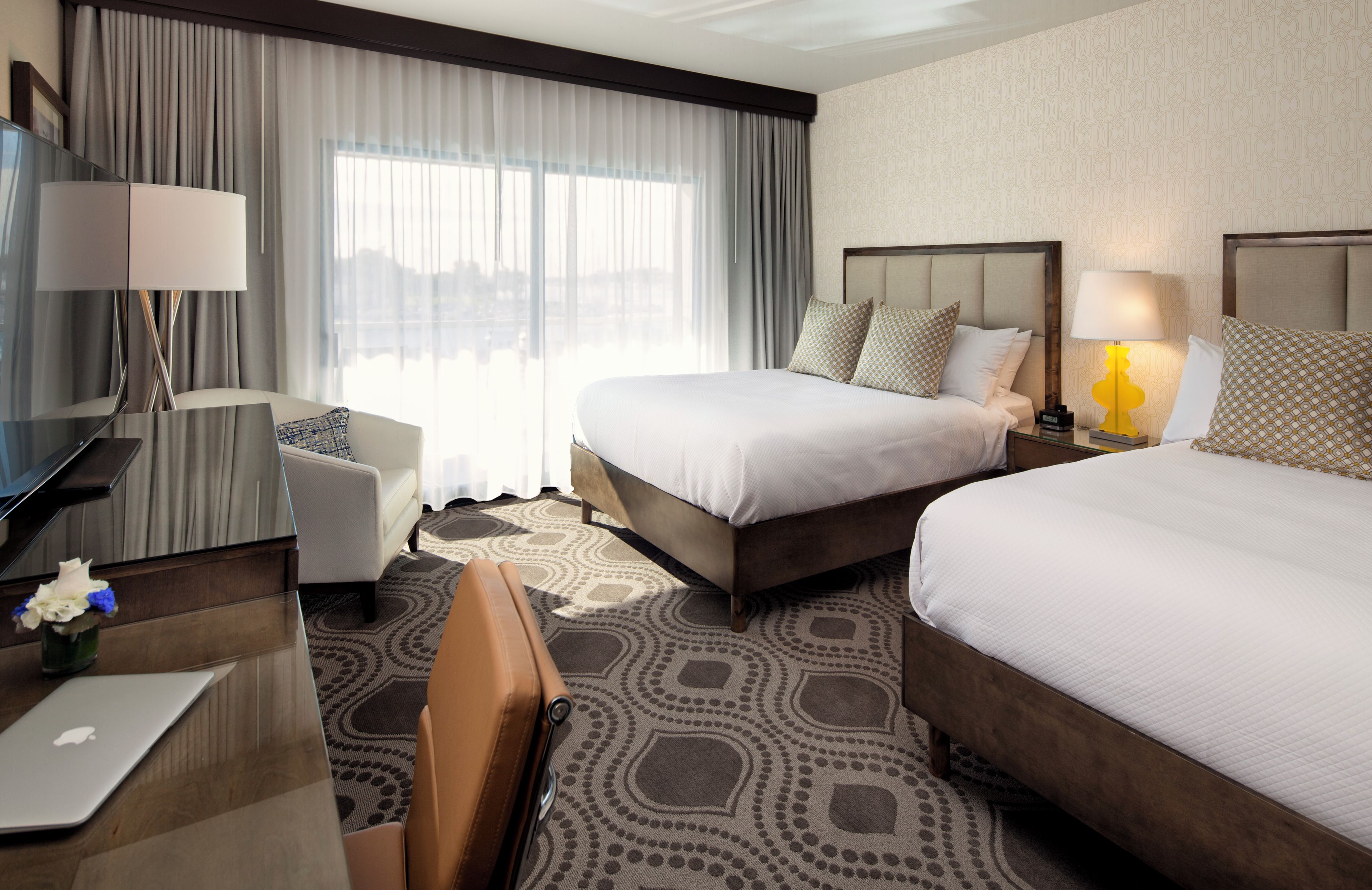 A hotel room with two beds, a desk with a laptop, a chair, and a TV.