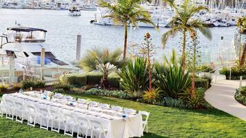 A table set for a meal with chairs, a marina with boats in the background, and palm trees.