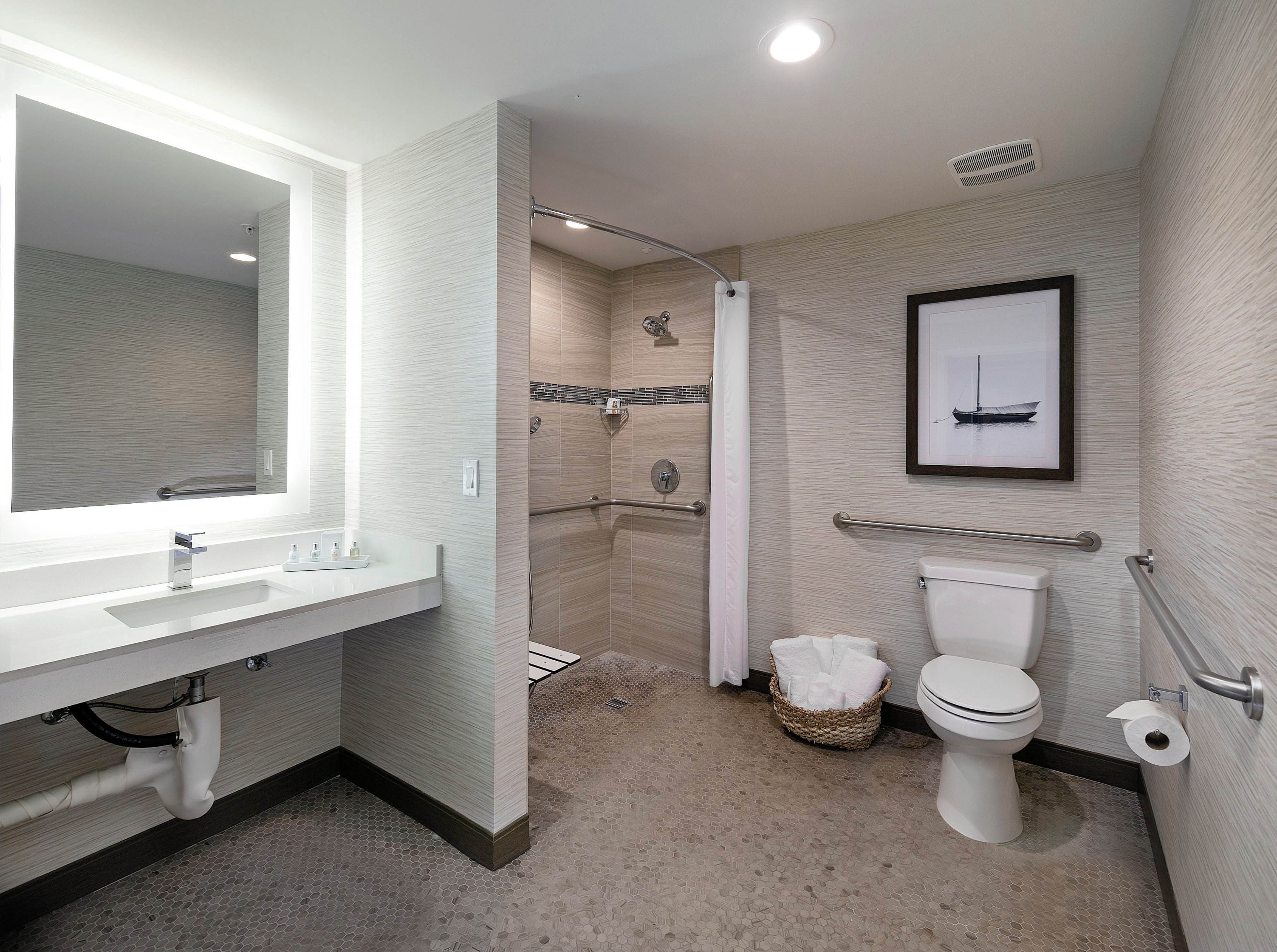 A modern bathroom with a large mirror, a shower with a glass door, a toilet, and a framed picture on the wall.