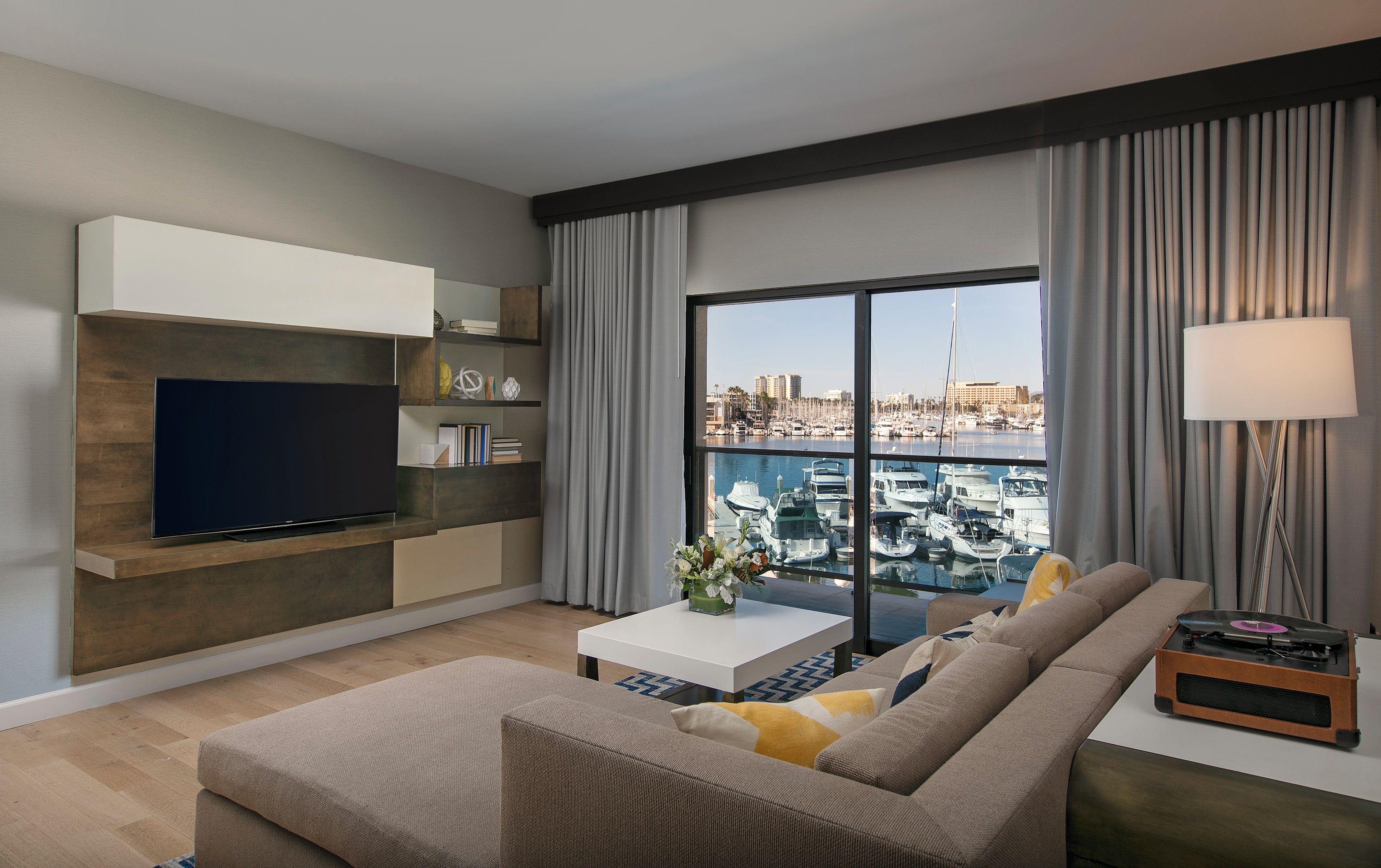 A modern living room with a flat-screen TV, a sofa, a coffee table, and a view of a marina.