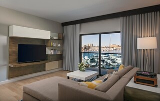 Una sala de estar moderna con una televisión de pantalla plana, un sofá, una mesa de centro y vista a un puerto deportivo.