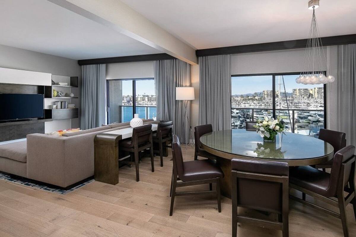 A modern hotel room with a sofa, dining table, chairs, and a TV.