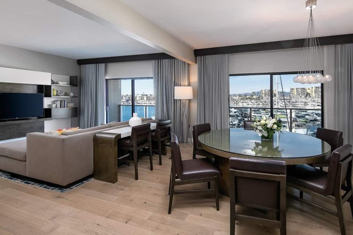 A modern hotel room with a sofa, dining table, chairs, and a TV.