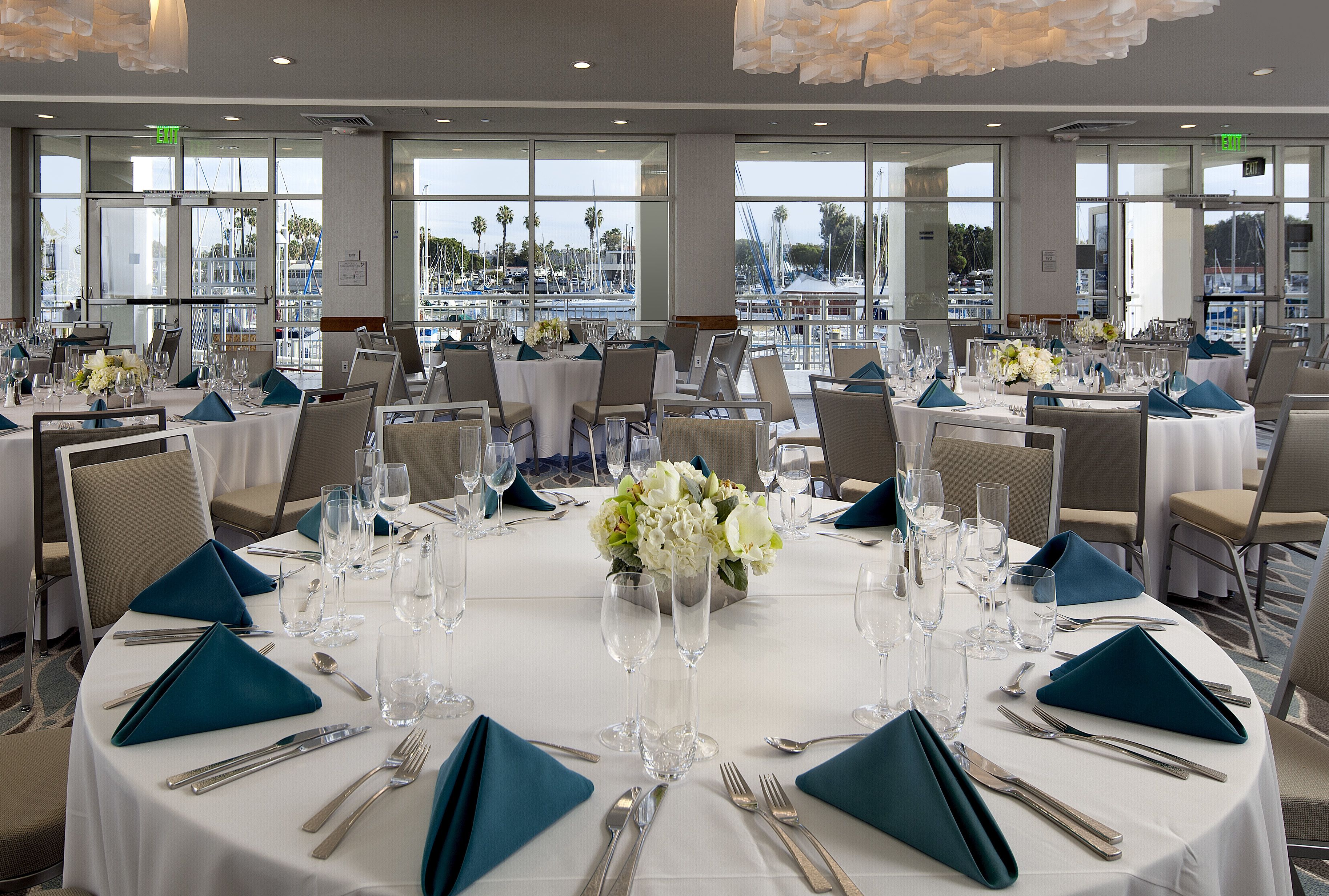 Une salle de banquet avec des tables rondes dressées pour un événement formel, agrémentée de nappes blanches, de serviettes bleues et de verres transparents.