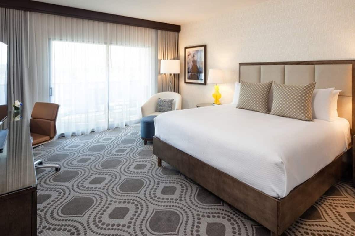 A hotel room with a large bed, a chair, a desk, and a window with curtains.