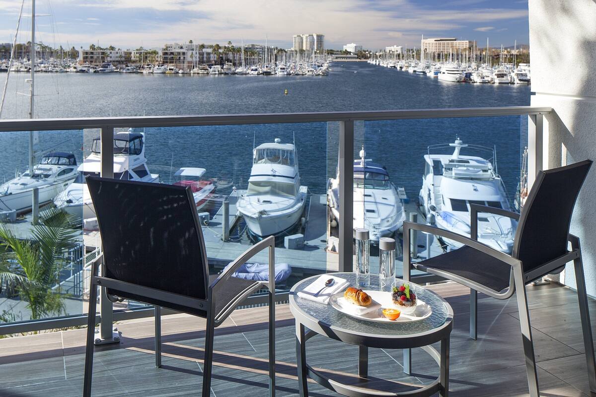 A balcony with two chairs and a table, overlooking a marina with boats and buildings.