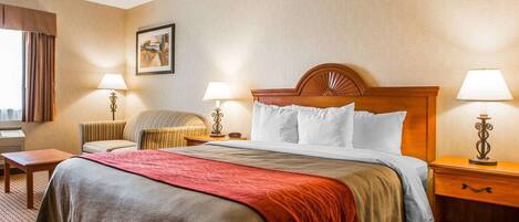 Habitación de hotel con una cama grande, dos mesitas de noche, una silla, un escritorio y una ventana con cortinas.