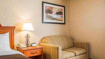 A hotel room with a bed, a nightstand with a lamp, a telephone, and a framed picture on the wall.