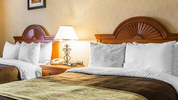 A hotel room with a large bed, a nightstand with a lamp and phone, and two framed pictures on the wall.