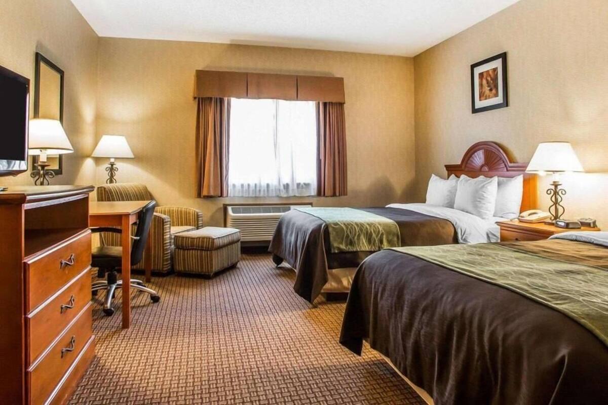 Habitación de hotel con cama, escritorio, silla, cómoda y aire acondicionado, además de televisor.