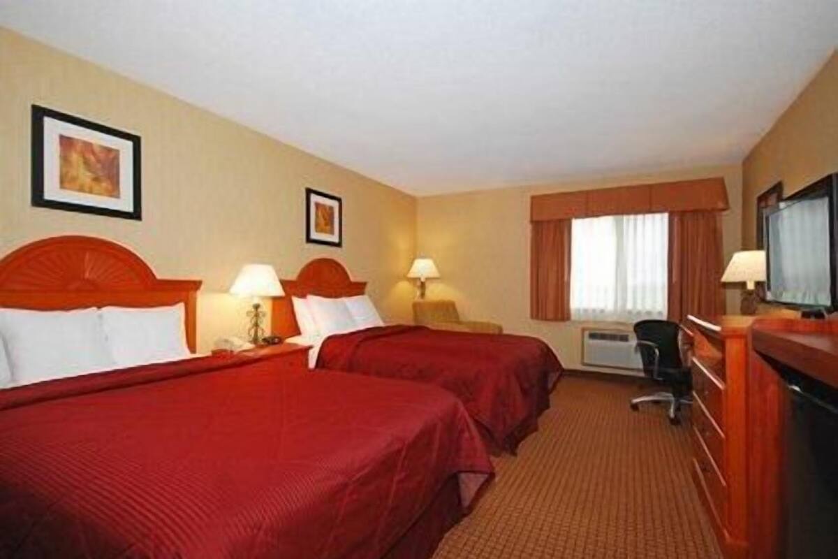 Habitación de hotel con dos camas, un escritorio, un televisor y una ventana con cortinas.