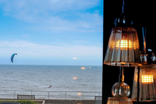 A coastal view with a parasail in the distance, a railing, and hanging lights.
