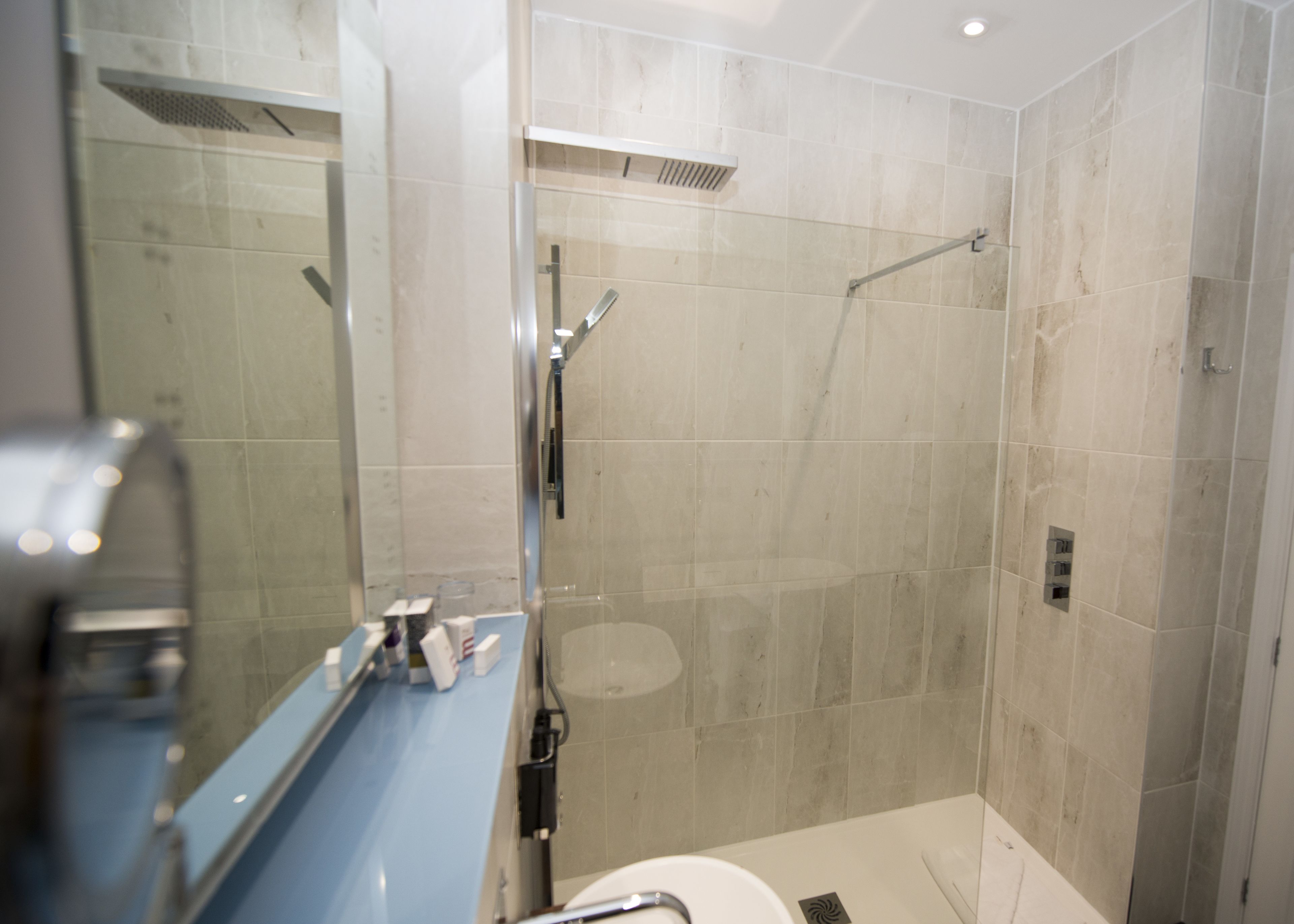 A modern bathroom with a glass-enclosed shower, a blue sink, and a large mirror.
