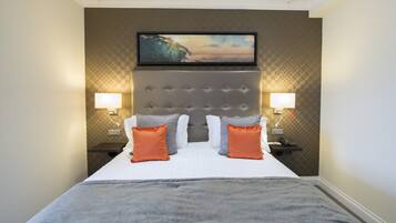 Habitación de hotel con una cama grande, dos mesitas de noche con lámparas, un televisor montado en la pared y un revestimiento de pared con textura.