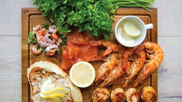 Une planche en bois sur laquelle sont disposés divers fruits de mer, notamment des crevettes, du saumon et des coquilles Saint-Jacques, le tout agrémenté de tranches de citron et de persil.
