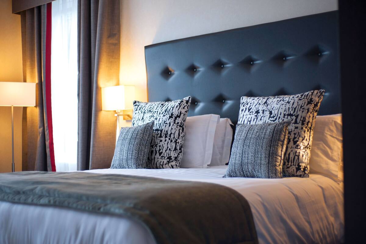 Une chambre d’hôtel avec une tête de lit capitonnée, des coussins à motifs et une lampe de chevet.