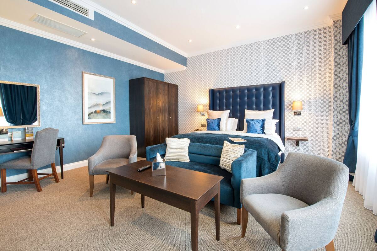 Une chambre d’hôtel avec un grand lit, deux fauteuils, un bureau et une table de chevet.