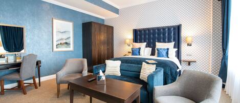 Una habitación de hotel con una cama grande, dos sillones, un escritorio y una mesita de noche.