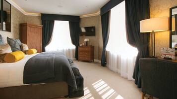 A hotel room with a large bed, a wooden dresser, a desk with a lamp, and a flat-screen TV mounted on the wall.