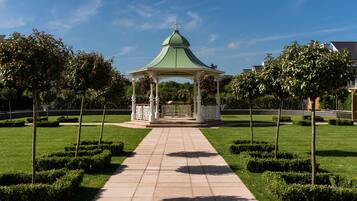 A gazebo with a green roof and white columns, surrounded by well-manicured hedges and trees.