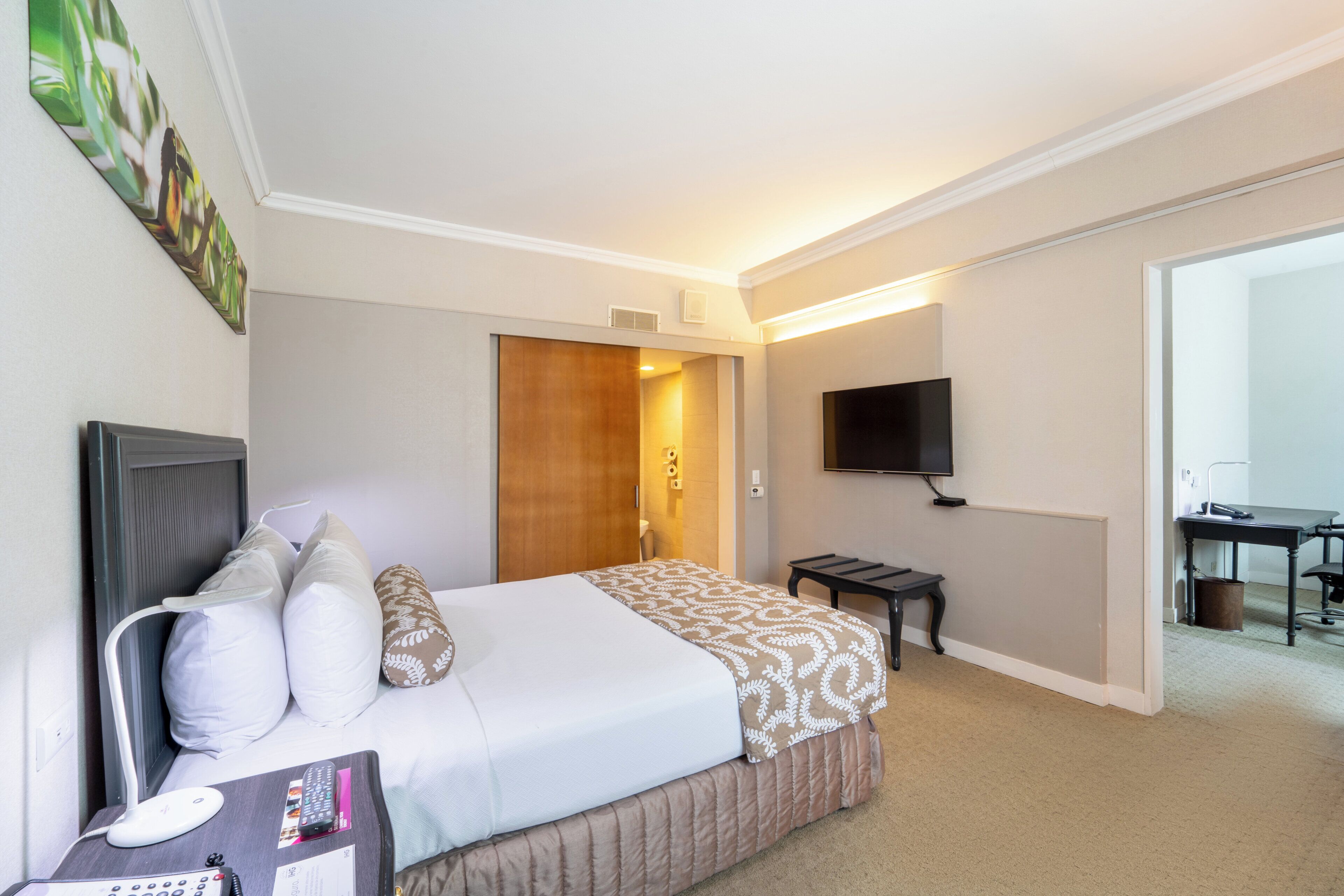 A hotel room with a bed, bedside table, TV, and a desk with a chair.