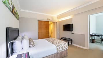 A hotel room with a bed, bedside table, TV, and a desk with a chair.